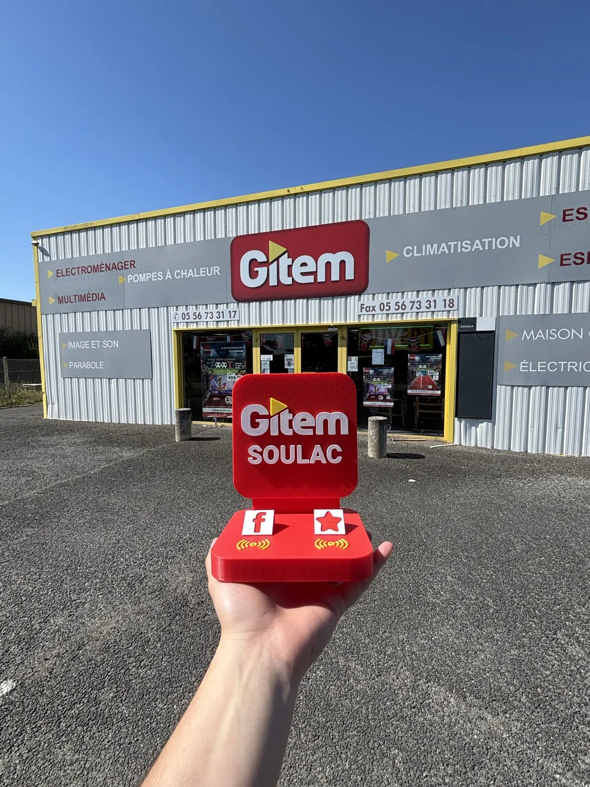 Stand NFC Filon Médoc aux couleurs Gitem Soulac, tenu en main devant la façade du magasin, avec ses logos réseaux Facebook et avis Google